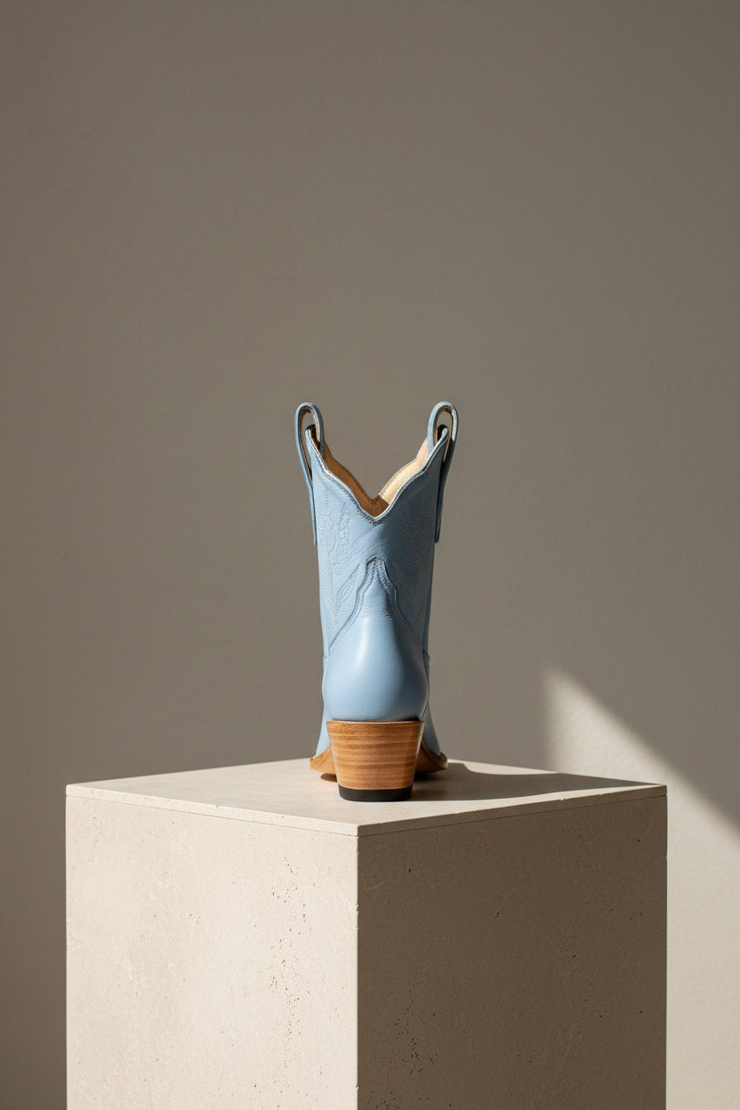 Blue cowboy boot on a beige pedestal against a gray background