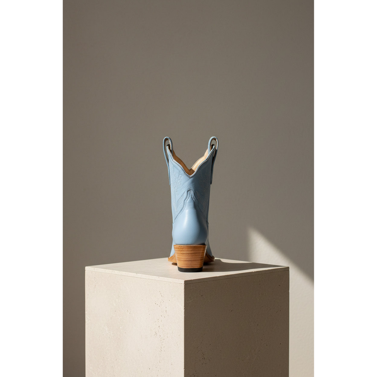 Powder blue boot in rear view on a stone pedestal