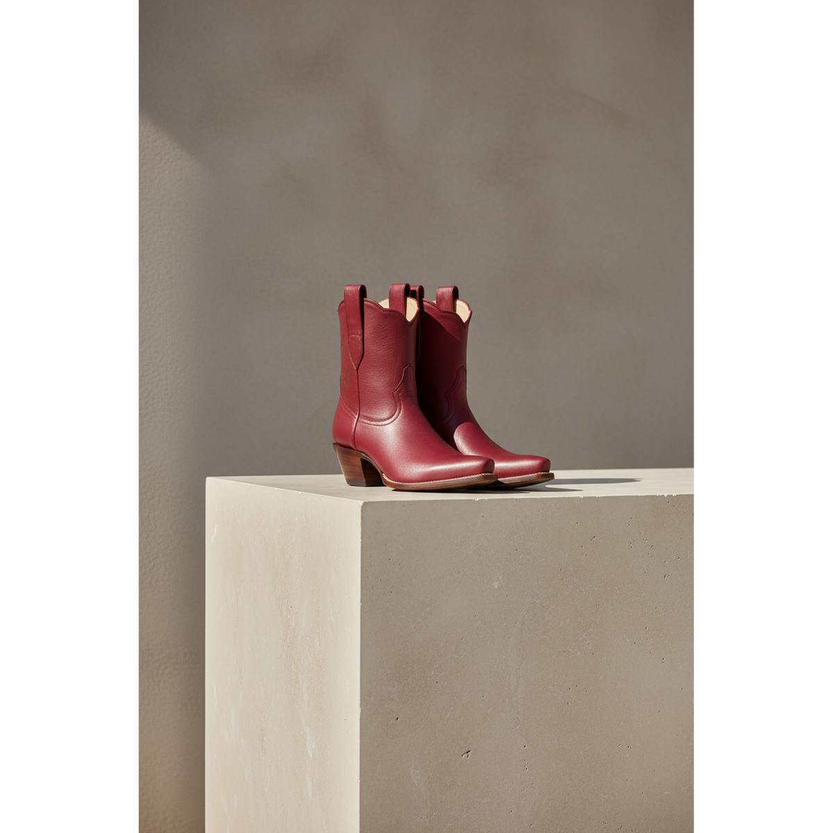 Pair of maroon Mariposa boots on a rectangular pedestal.