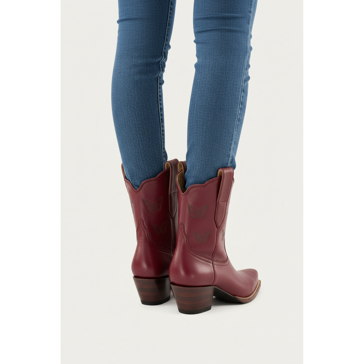 Rear view of maroon Mariposa boots worn with blue trousers.