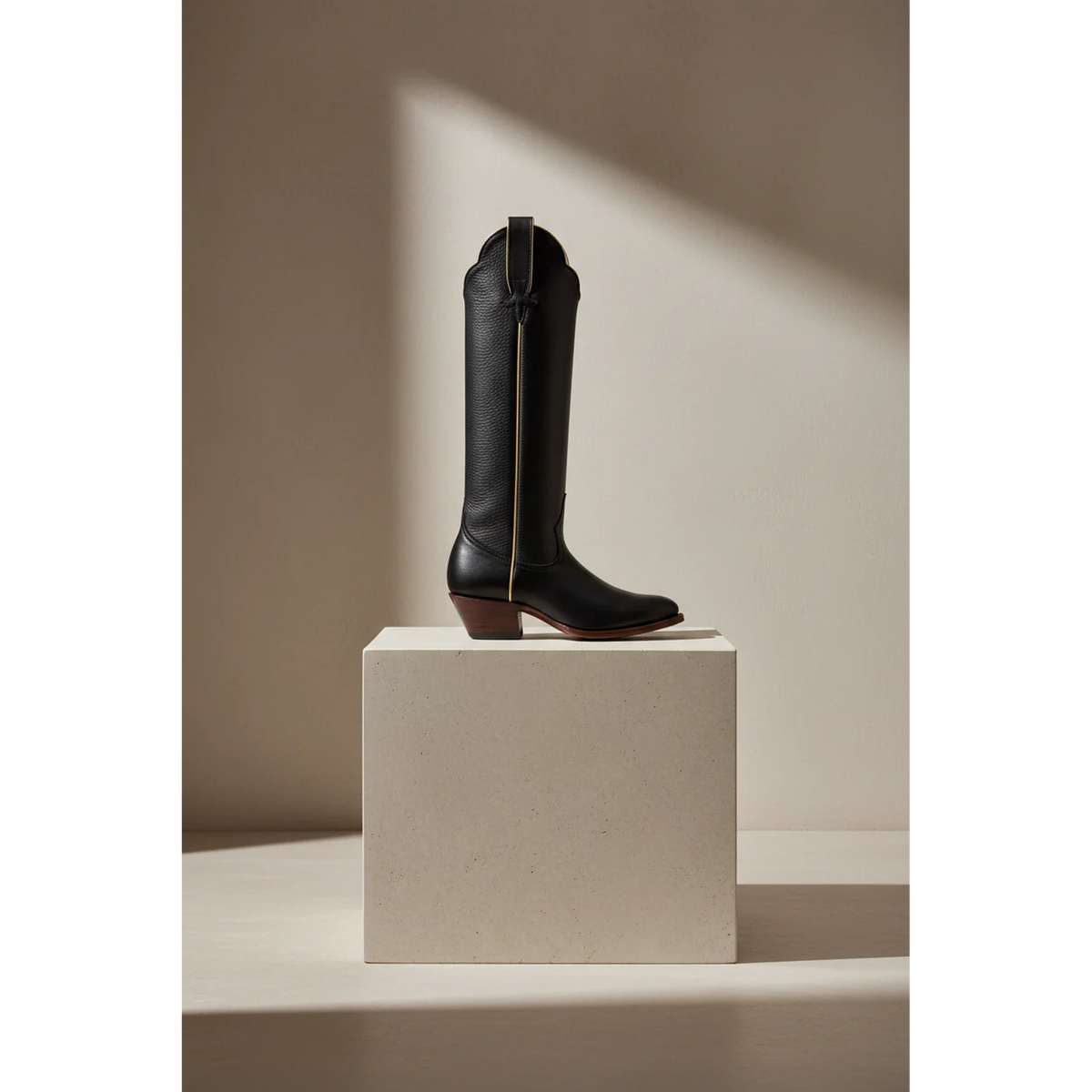 Black and Gold McCall western boot with gold piping on a stone pedestal