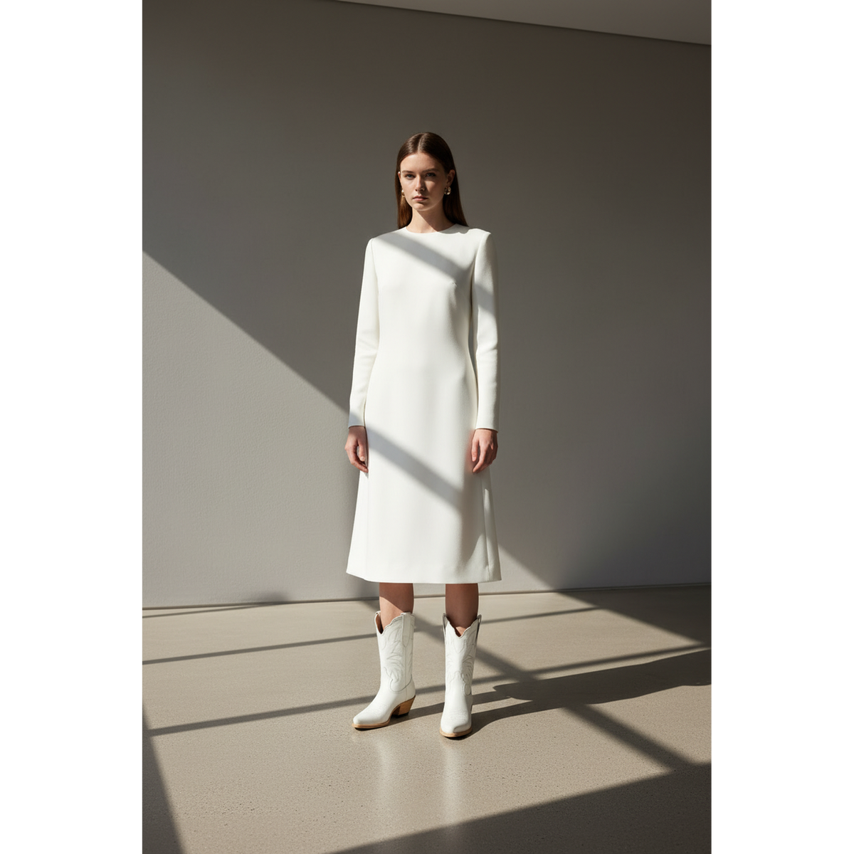 Woman wearing white midi boots with a white dress in angular window light.