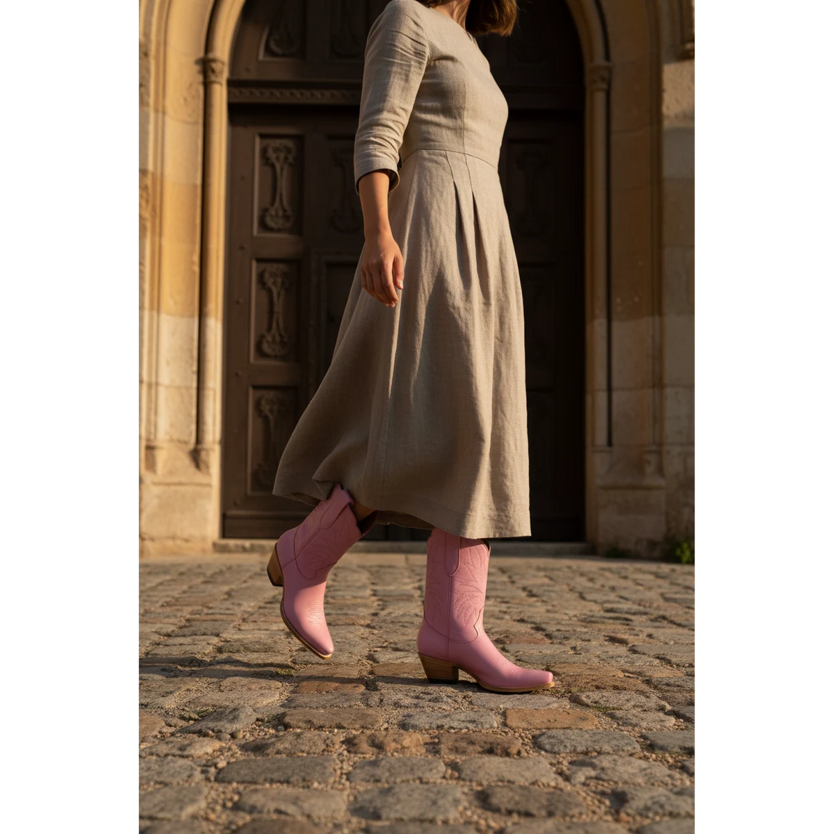 Pink midi boots styled with a taupe dress on a cobblestone street.