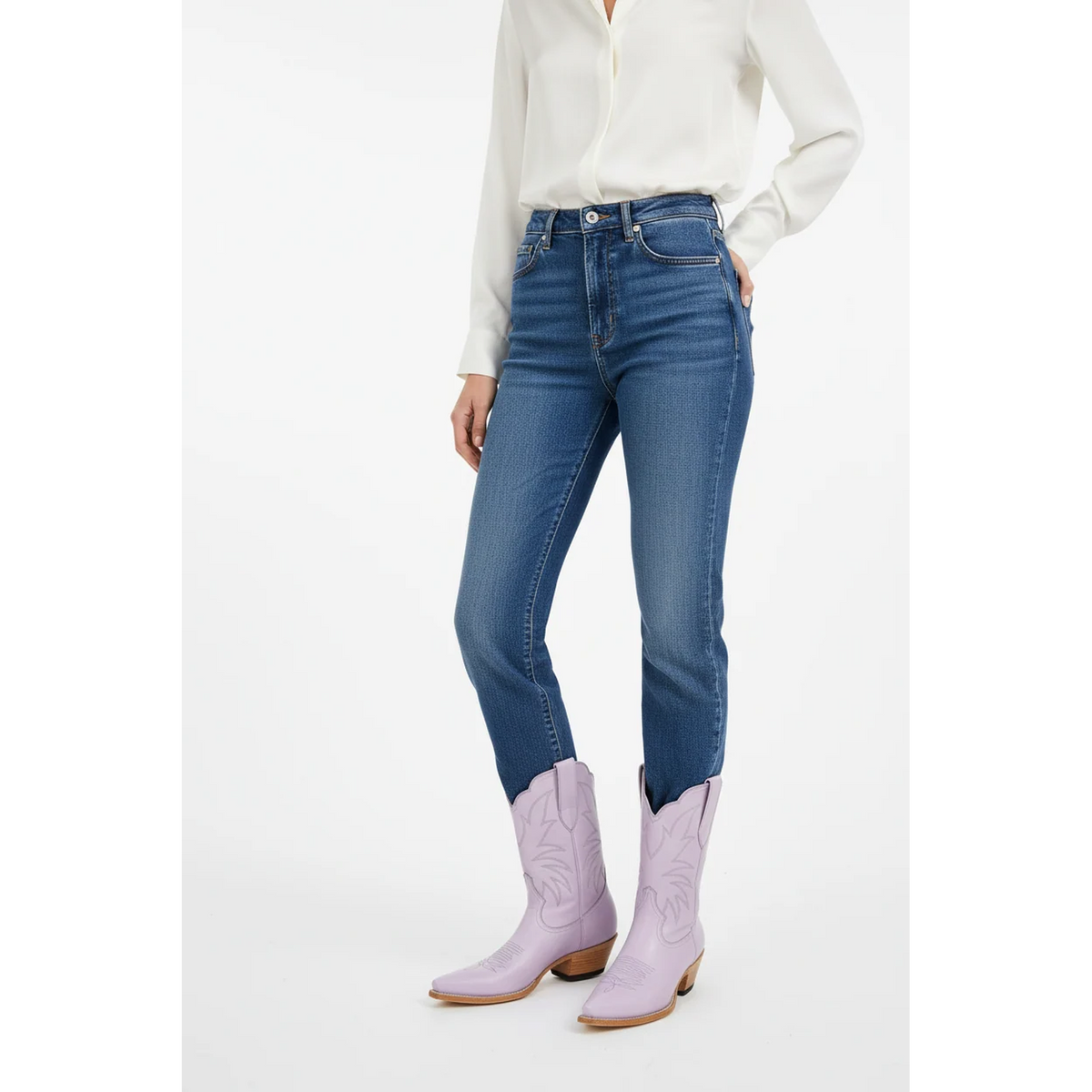 Person wearing blue jeans and lavender cowboy boots on a white background