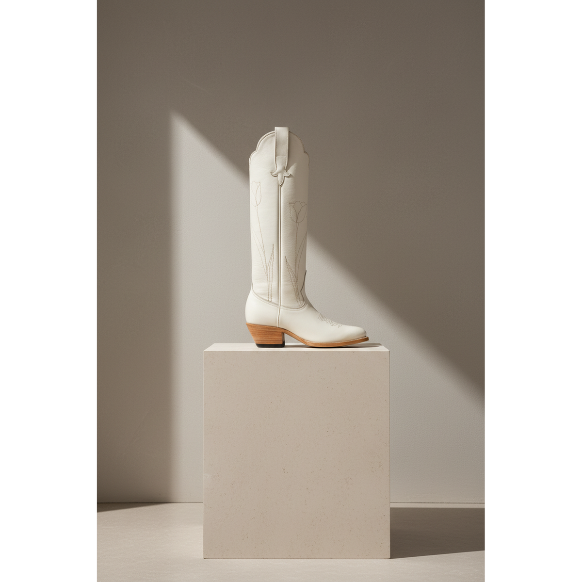 Bone Tulip boot with tonal tulip detailing, side view on a stone pedestal