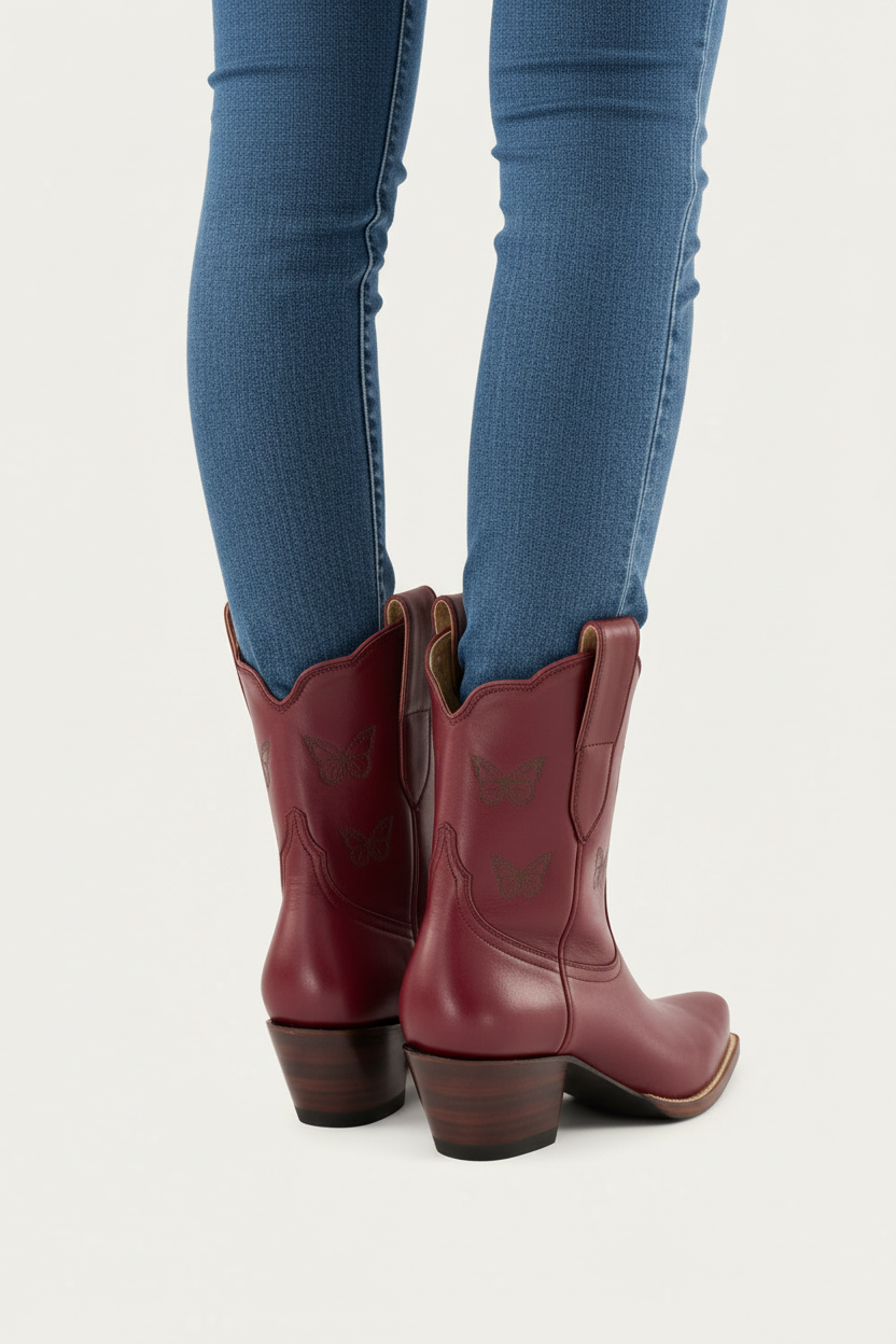 Red burgundy maroon wine cowboy boots worn with blue jeans on a light gray background