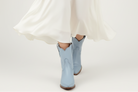 Person wearing light blue rain boots with a white skirt on a plain background
