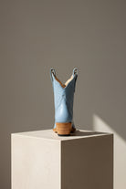 Blue cowboy boot on a beige pedestal against a gray background