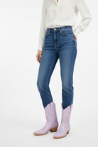 Person wearing blue jeans and lavender cowboy boots on a white background