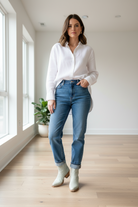 Woman wearing a white shirt, blue jeans, and white boots in a bright room.