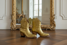 Gold alligator exotic luxury cowgirl short cowboy boots on a wooden floor with an ornate gold mirror in the background.