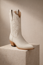 ivory cream off White cowgirl cowboy boot with brown sole on a beige block against a beige background bridal 
