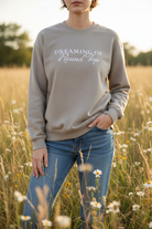 Person wearing a beige Dreaming of Round Top sweatshirt with text in a field