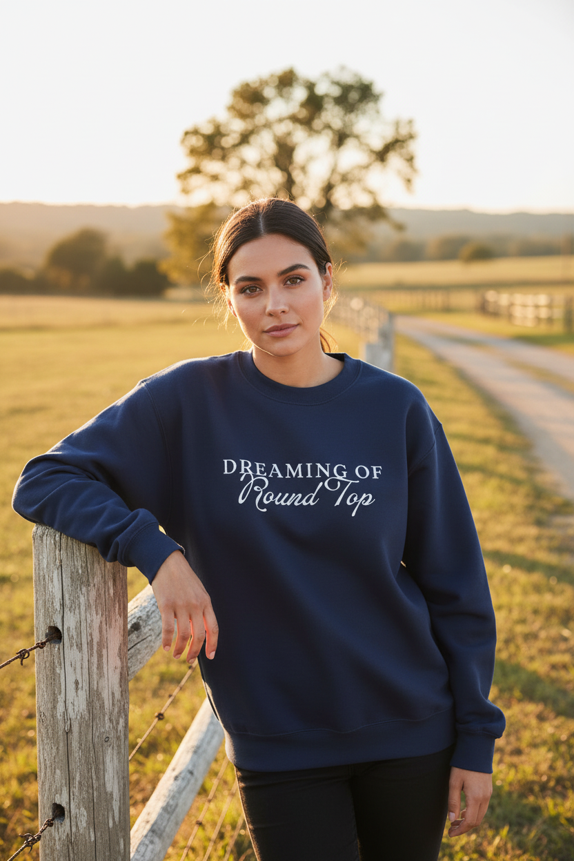 Woman wearing a navy blue Dreaming of Round Top sweatshirt with text, standing in a field.