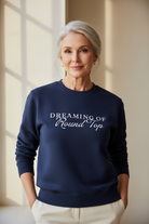 Woman wearing a navy blue sweatshirt with 'Dreaming of Round Top' text, standing in a softly lit room.