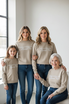 Four women of different generations wearing matching beige sweatshirts with text Dreaming of Round Top embroidered, standing close together in a bright room.