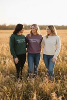 Three women standing in a field wearing sweatshirts with text Dreaming of Round Top embroidered