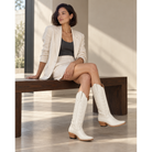 Woman in an ivory jacket and shorts wearing ivory boots.