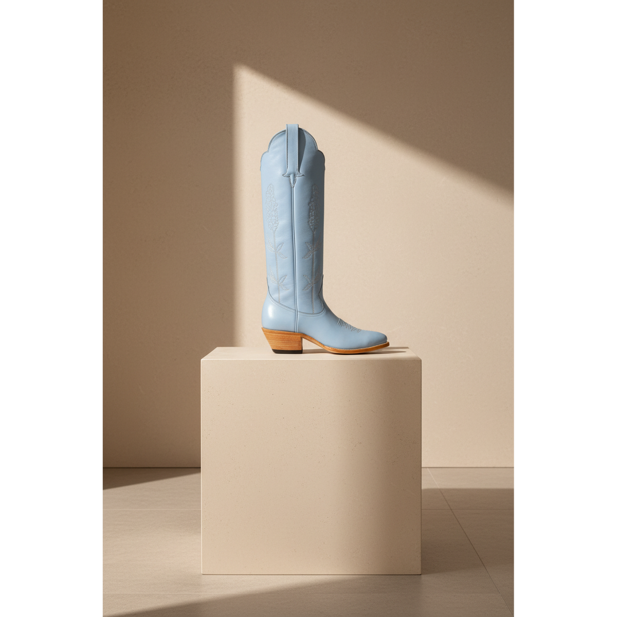 Powder Blue Bluebonnet tall western boot with floral detail on a stone pedestal