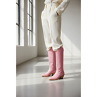 Pink Buttercup boots worn with a cream outfit beside a window