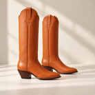 Pair of chestnut tall boots in a staged scene.