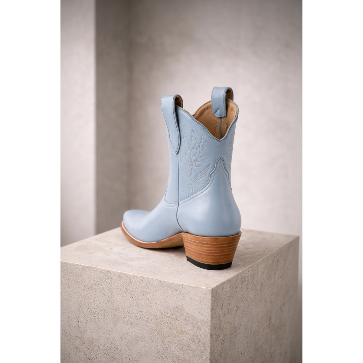 Powder blue boot in rear three-quarter view on a stone pedestal