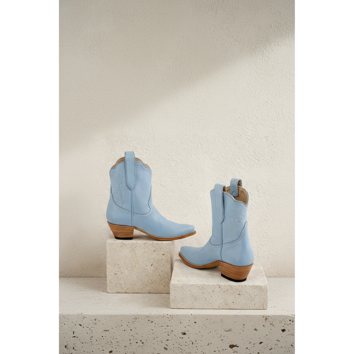 Pair of powder blue boots displayed on stone blocks