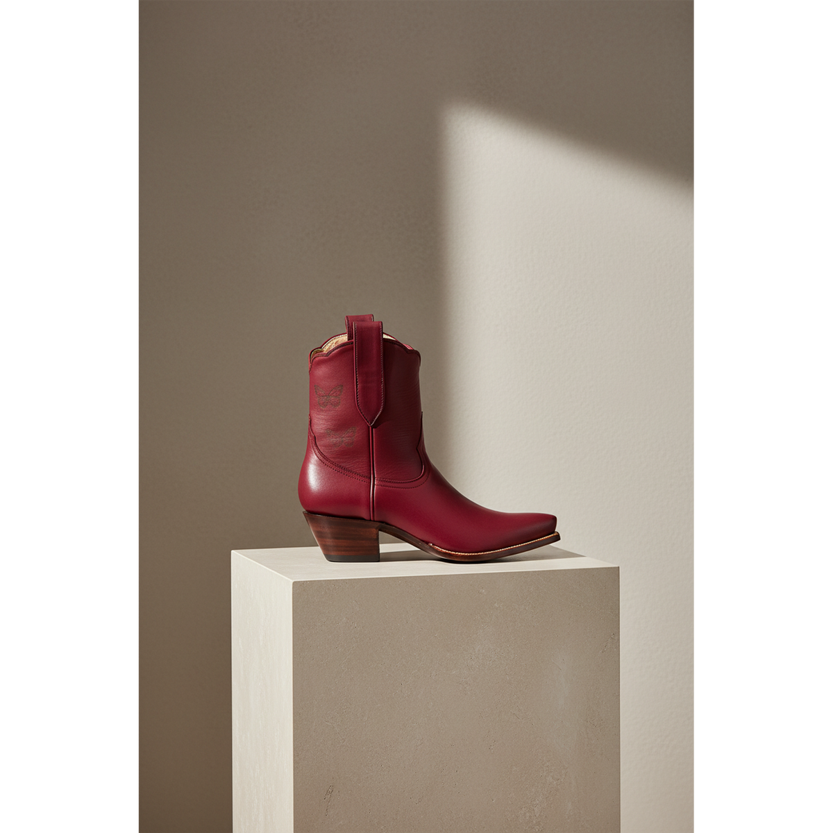 Maroon Mariposa boot in side view on a rectangular pedestal.