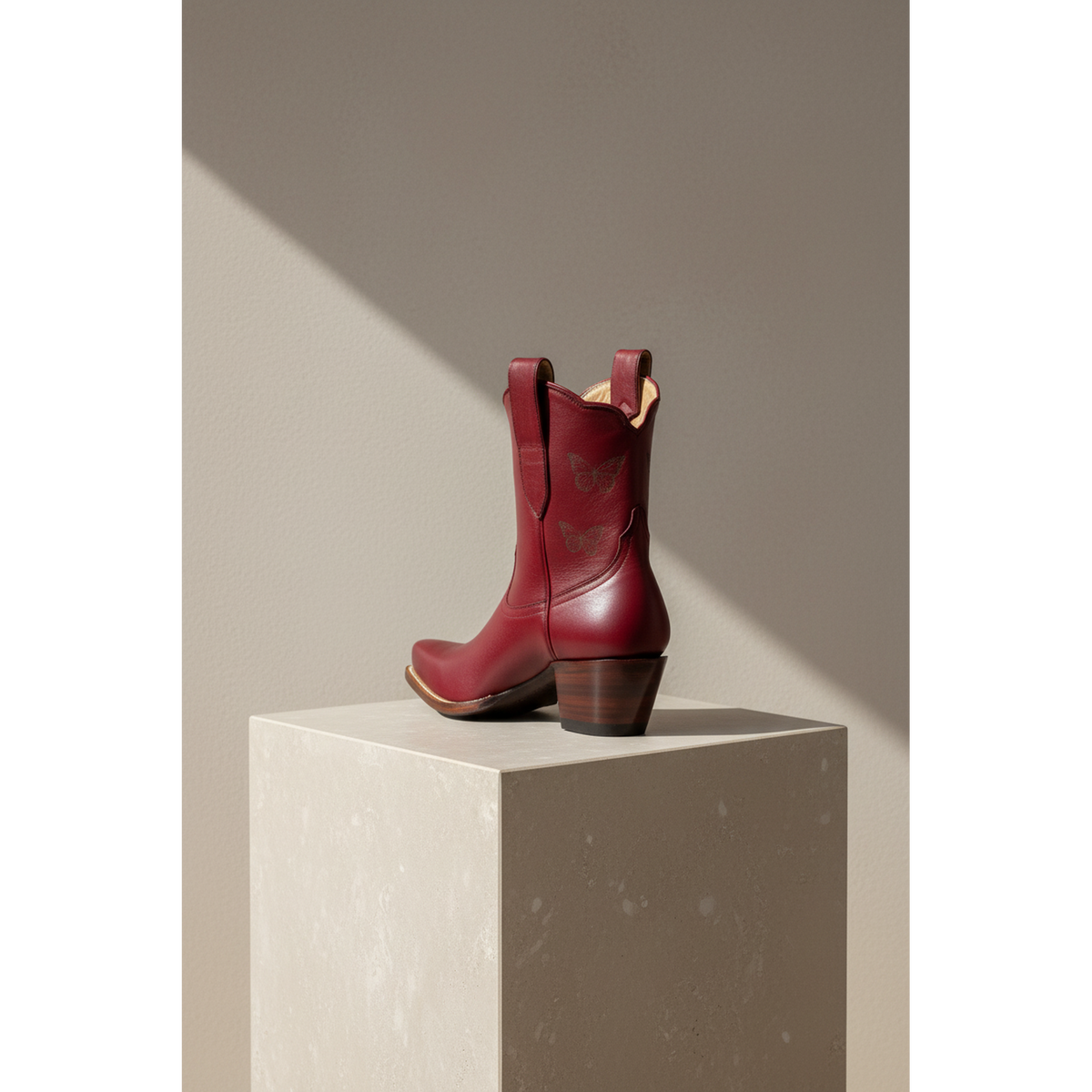 Rear and side views of maroon Mariposa boots on a pedestal.