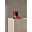 Pair of maroon Mariposa boots on a rectangular pedestal.