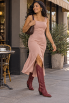 Maroon boots, blush silk café departure. AI-generated editorial image.