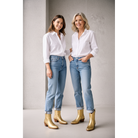 Two women wearing metallic-gold boots with cuffed jeans and white shirts