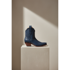 Navy Payton boot, side view on a pedestal in a sunlit room.