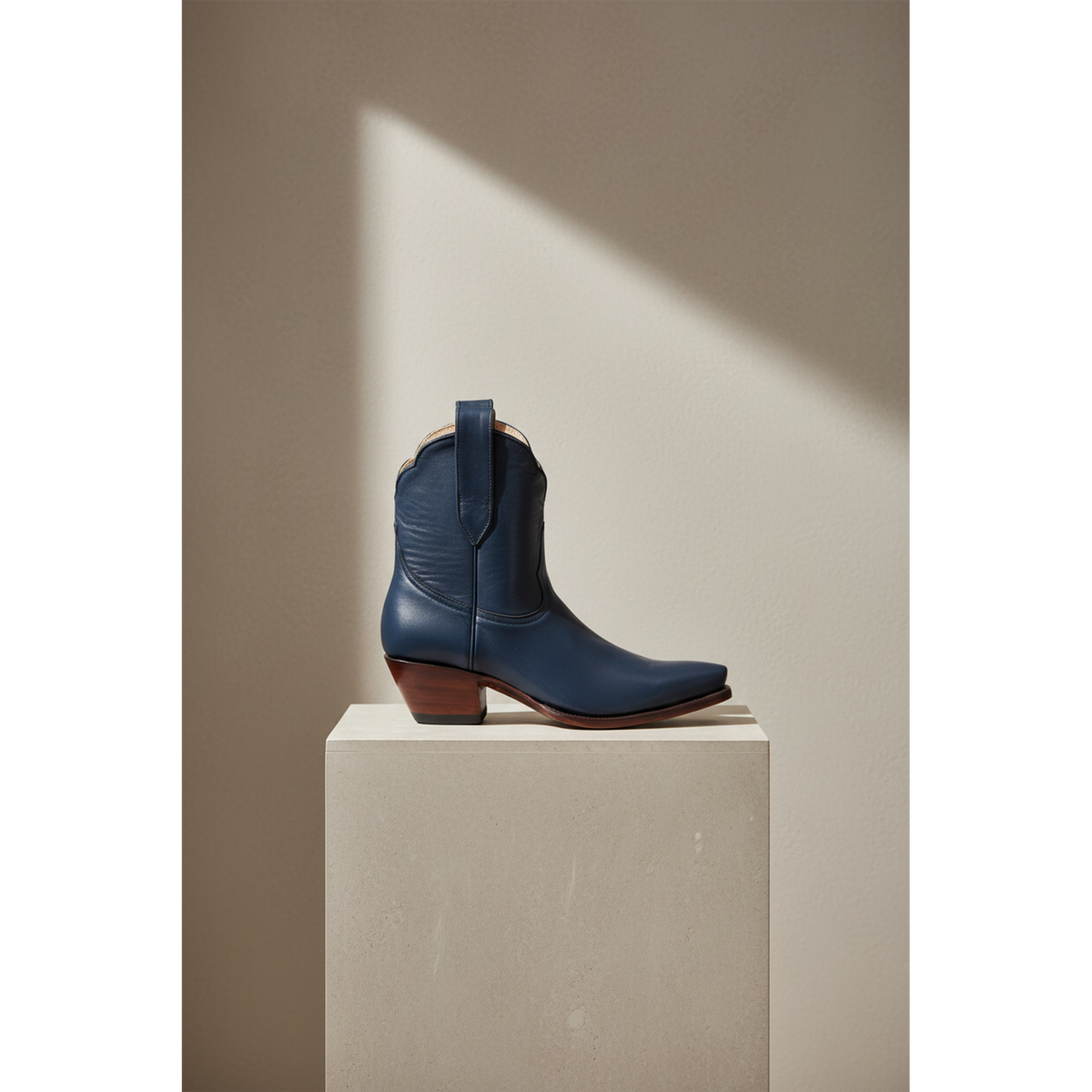Navy Payton boot, side view on a pedestal in a sunlit room.