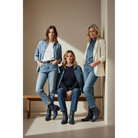Three women in blue and neutral outfits wearing dark boots in a studio.