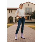 Woman wearing lavender boots, jeans and a white top on a brick courtyard path.