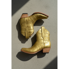 Gold American alligator crocodile-patterned boots with brown soles on a concrete surface