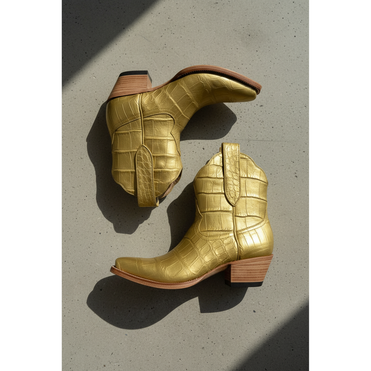 Gold American alligator crocodile-patterned boots with brown soles on a concrete surface