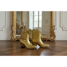 Gold alligator exotic luxury cowgirl short cowboy boots on a wooden floor with an ornate gold mirror in the background.