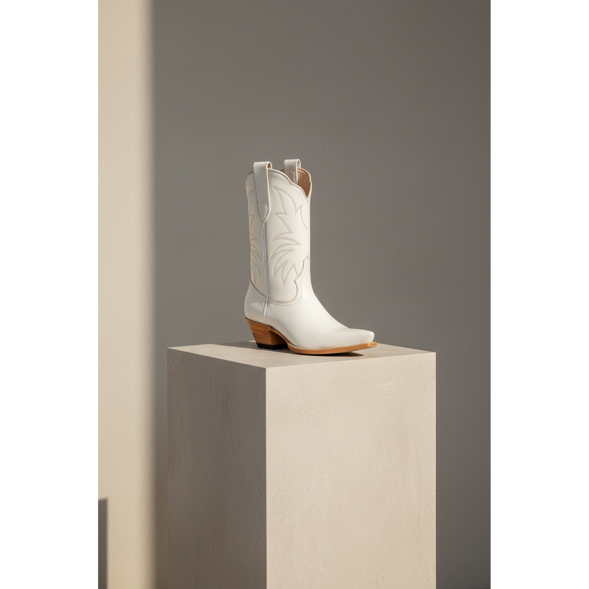 Three-quarter view of the Bone Marjorie Midi boot on a tall pedestal in soft window light.