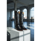 Pair of black cowboy boots on a white pedestal in a large room with arched windows.