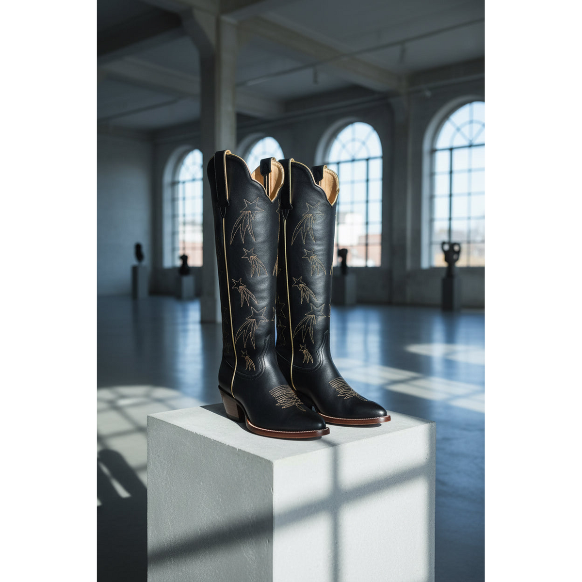 Pair of black cowboy boots on a white pedestal in a large room with arched windows.