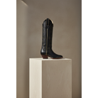 Tall boot displayed on a light pedestal, gallery view 1