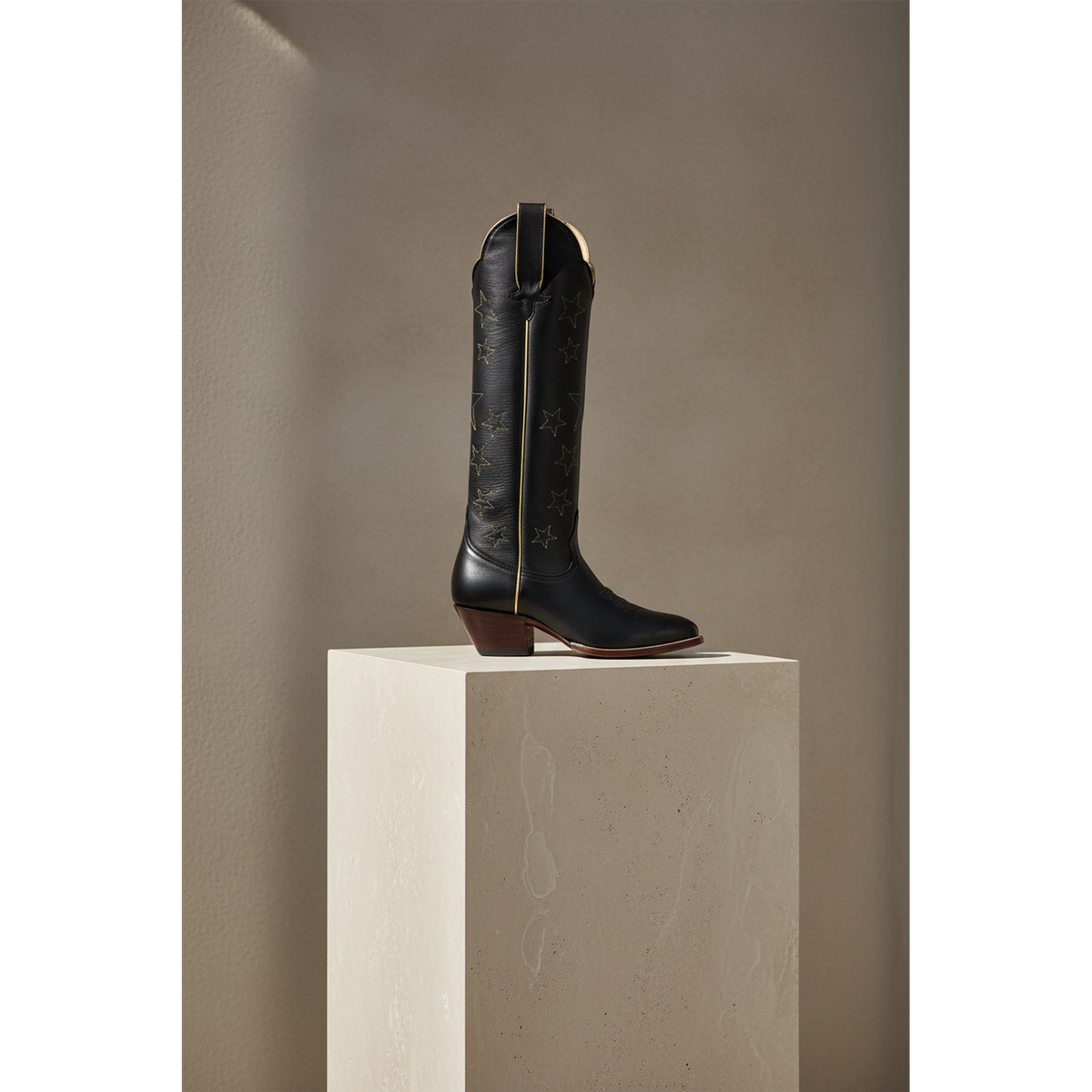 Tall boot displayed on a light pedestal, gallery view 1