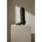 Tall boot displayed on a light pedestal, gallery view 2