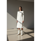 Woman wearing white midi boots with a white dress in angular window light.