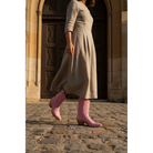 Pink midi boots styled with a taupe dress on a cobblestone street.
