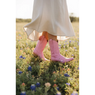 Pink midi boots beneath a flowing cream skirt in a wildflower field.