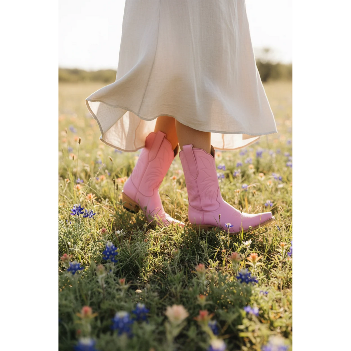 Pink midi boots beneath a flowing cream skirt in a wildflower field.