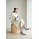 Woman seated on a wooden block wearing lavender boots and a cream dress.